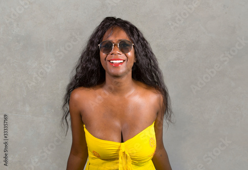young stylish and happy black African American woman in yellow dress and sunglasses posing confident and playful isolated on dark background looking at camera in cool attitude
