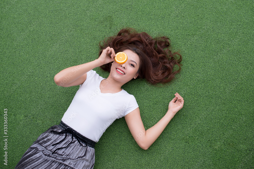 Φωτογραφία Young Asian woman enjoying the lying on her back on the green grass and hiding her eye with orange piece