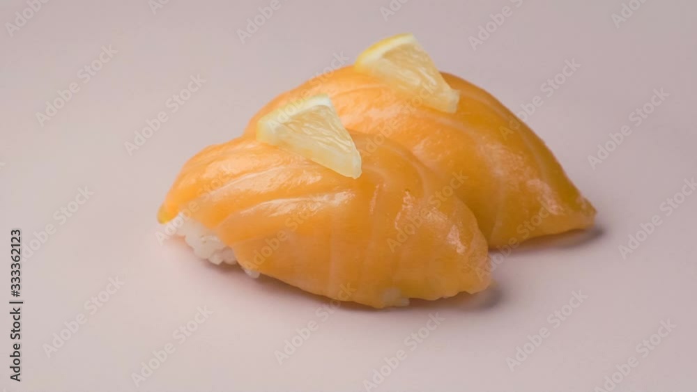 Two salmon sushi with lemon slices on the spinning pink plate.