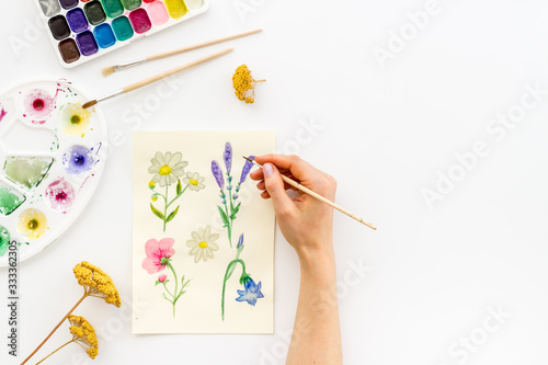 Painting. Female hands draw flowers on white background top-down copy space