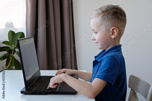 Distance learning online education. Cute caucasian boy doing homework on a computer while quarantine of epidemia corona virus photo