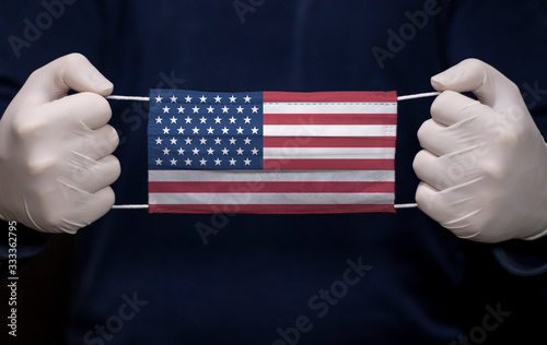 Health employee doctor holding medical face mask with USA flag. Coronavirus (COVID-19) pandemic affects the country.