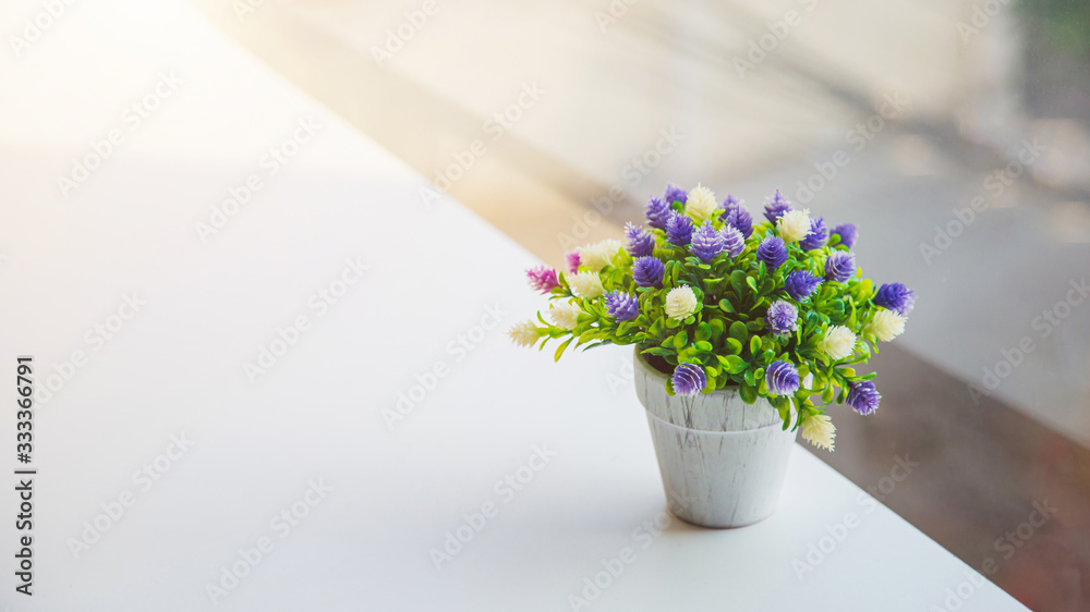 An artificial globe amaranth flower in vase on table with house and green tree blurred background with pastel color tone.