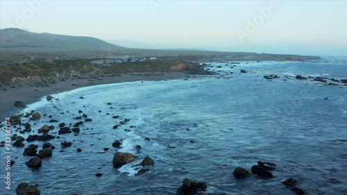 Aerial drone push in shot of cars parked at a vista point overlooking the waves hitting the rocks in San Simeon, California, USA photo