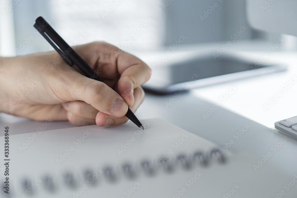 Man writes with a pen in diary in a sunny office, business and education concept. Close up Man writes with a pen in diary in a sunny office, business and education concept. Close up