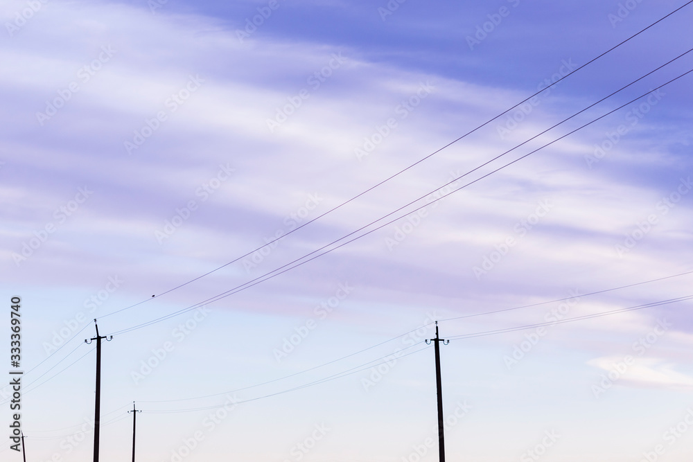 Poles and wires against the blue spring sky. Electricity pole with the blue cloudy sky background. 