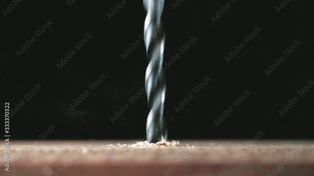 Electric drill bit drills a hole in the board. Joinery and construction work close up. Wood chippings fly off a metal drill. Handyman bores holes into a wooden board.  