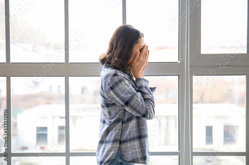 Depressed young woman near window