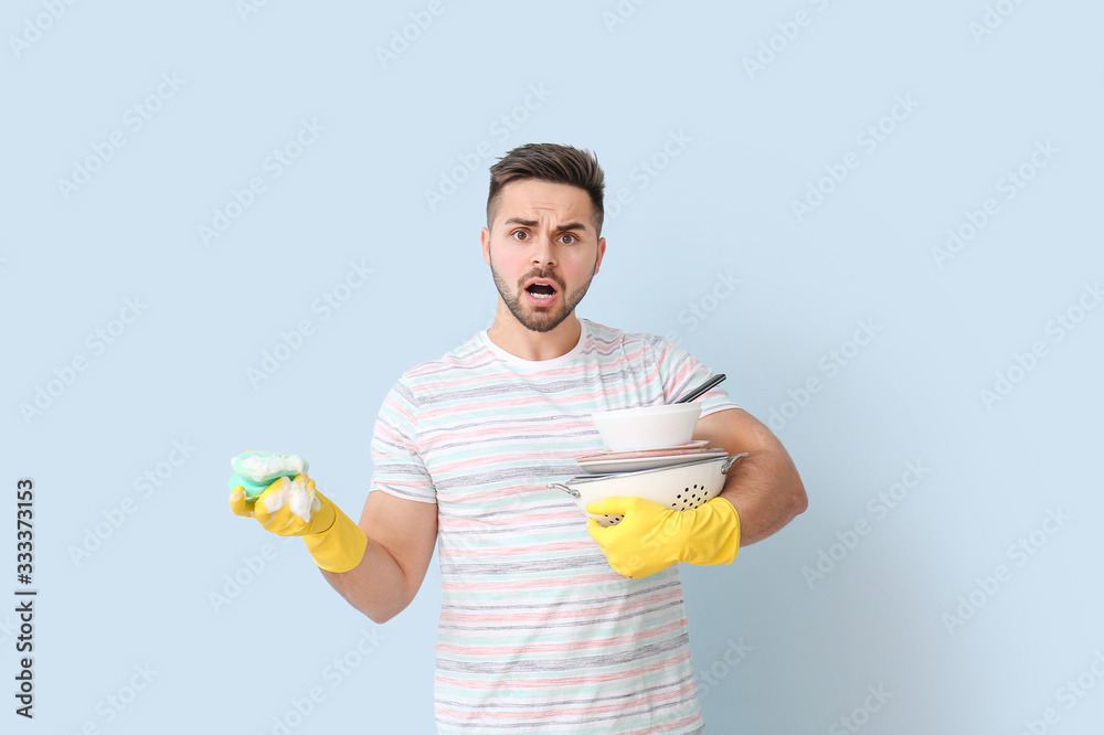 Displeased man with dirty dishes and sponge on color background Displeased man with dirty dishes and sponge on color background