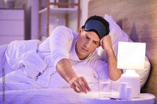 Young man taking pills for insomnia in bedroom