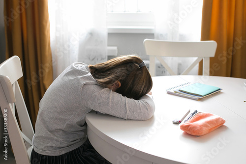Pretty cute schoolgirl 7-8 years old sleeping on table. Home school, online education, home education, quarantine, coronavirus concept photo