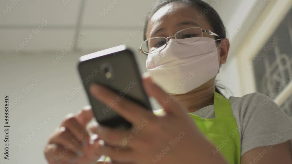 Housewife wearing protective mask using mobile smart phone for communication and watching on social online at home. Data tracking and daily news with mobile phone during Covid-19 situation. Housewife wearing protective mask using mobile smart phone for communication and watching on social online at home. Data tracking and daily news with mobile phone during Covid-19 situation.