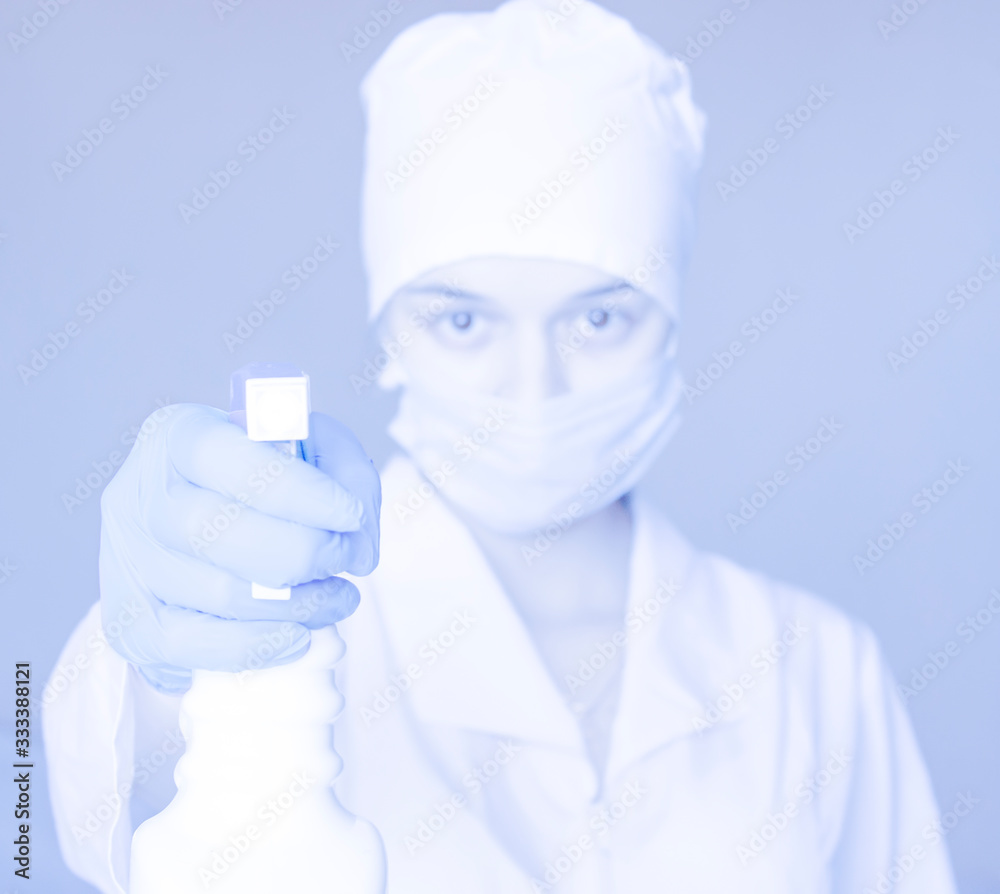 A nurse in a dressing gown with antiseptic spray looks at the screen. Disinfection of hands and objects. Prevention and protection from viral diseases. A nurse in a dressing gown with antiseptic spray looks at the screen. Disinfection of hands and objects. Prevention and protection from viral diseases.