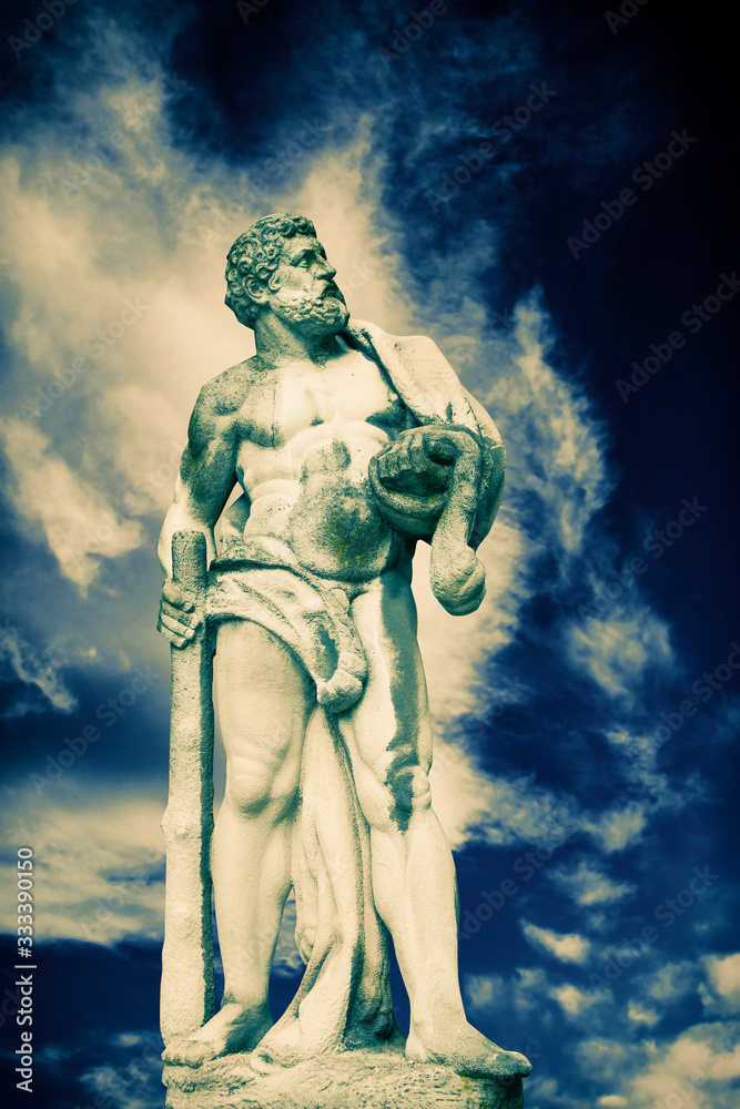 Ancient stone statue of Hercules against dramatic view of cloudy sky as symbol of power and strength. Ancient stone statue of Hercules against dramatic view of cloudy sky as symbol of power and strength.