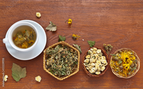 Top view of a cup of healing herbal tea for cough and cold from dried flowers of calendula  chrysanthemum and cinquefoil. Baskets with dried medicinal herbs.  Tea are useful for coronavirus infection