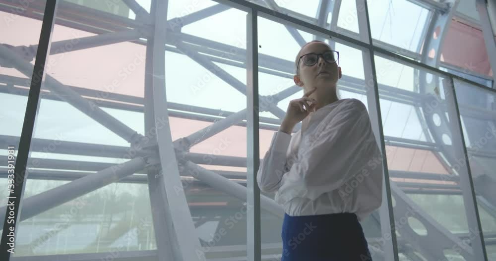 Serious business lady standing near window and thinking