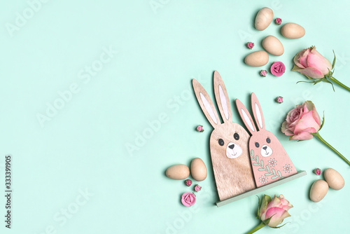 Wooden easter eggs and easter bunnies surrounded by beautiful pink roses, on a green background. Celebrate easter with this fun easter flat lay background.
