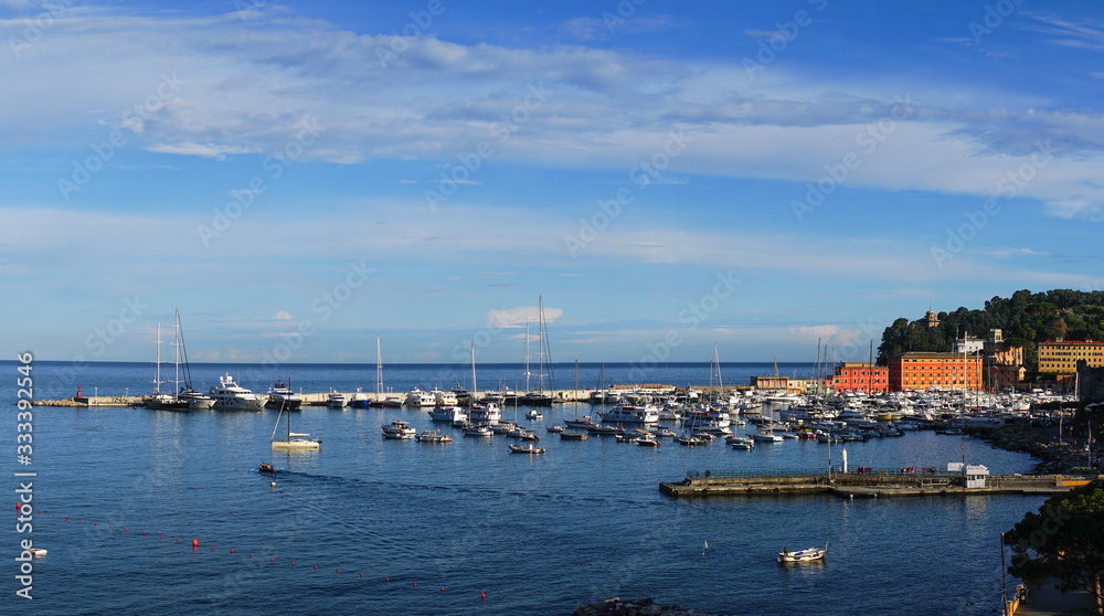 Wide panoramic view of luxury yachts and sailing boats moored in harbor of Santa Margherita Ligure, Italian Riviera. Beautiful mediterranean landscape with cloudy blue sky.