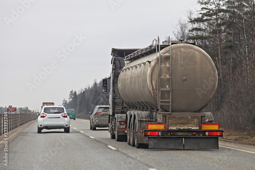 Dirty barrel fuel tank truck on suburban two-lane road at Spring day on forest background, liquid cargo transportation