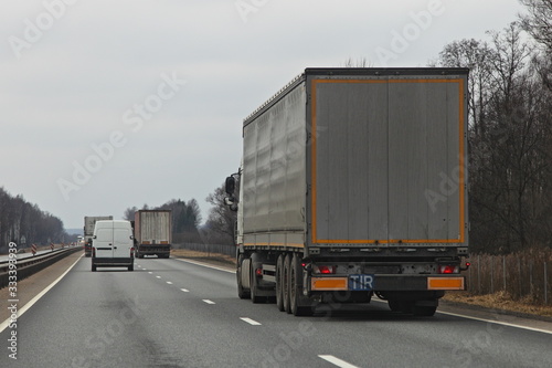 Semi truck van move on two lane suburban asphalt highway at spring day, rear-side view – international logistics, cargo transportation, trucking industry