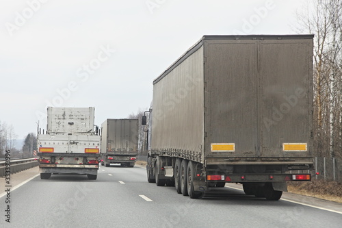 Long vehicle semi trucks overtaking moving on a two-lane asphalted country road at spring day, rear view