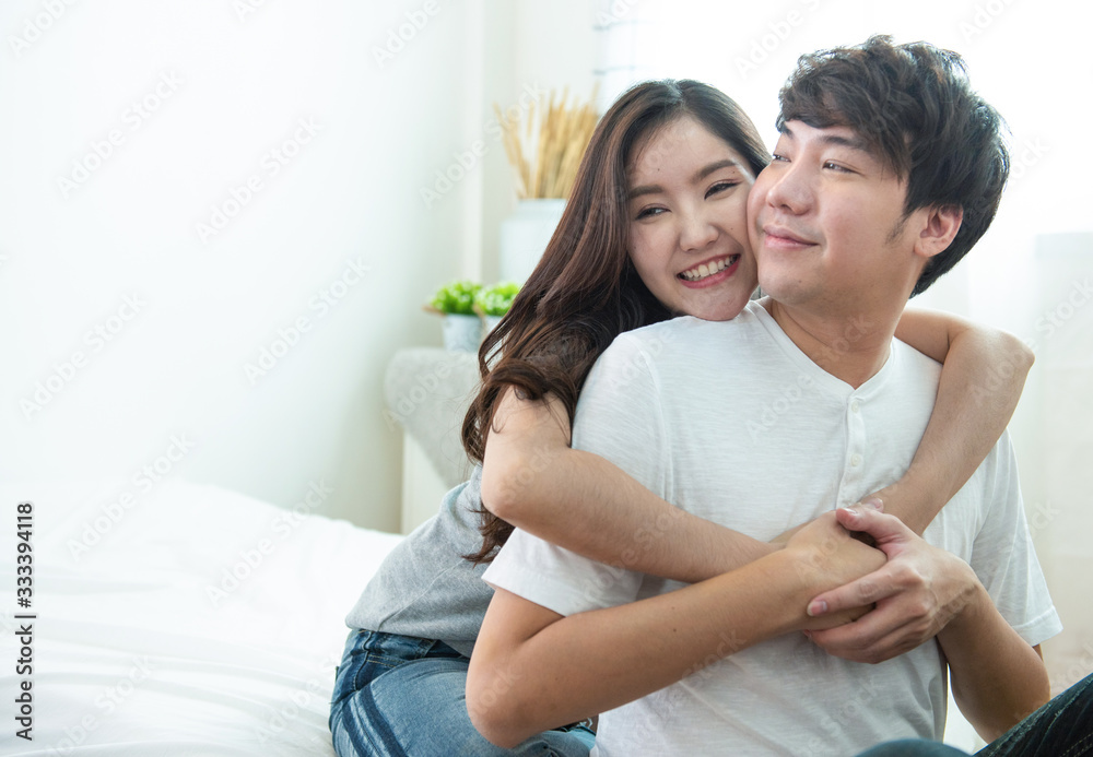 selective focus on woman face with portrait of young asian couple girl piggyback man from back on bed,romantic asia people in love hugging while sitting in bed,valentine day concept with copy space. selective focus on woman face with portrait of young asian couple girl piggyback man from back on bed,romantic asia people in love hugging while sitting in bed,valentine day concept with copy space.