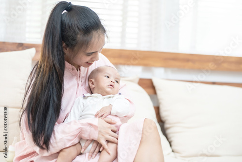 family, child and parenthood concept - happy beautiful young asian mother smiling hugging holding newborn baby in her arms at home. Mother’s day banner with copy space for advertise