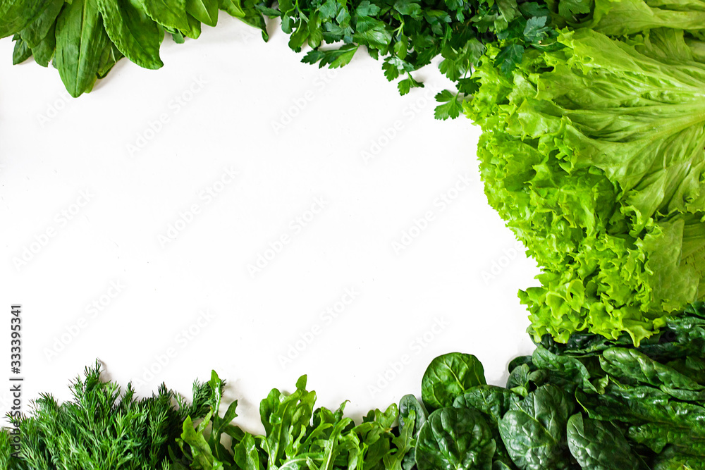 Obraz premium Green vegetables. Green fruits and vegetables on a white background. Apples, parsley, spinach, arugula and lettuce on a white background. Top view. Spinach and vegetable smoothies with copy space