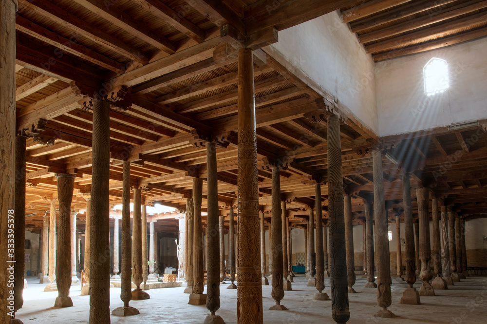 Main hall of Juma mosque (10th and 18th centuries) with old wooden pillars and sunbeams from the window. Khiva, Uzbekistan, Central Asia.