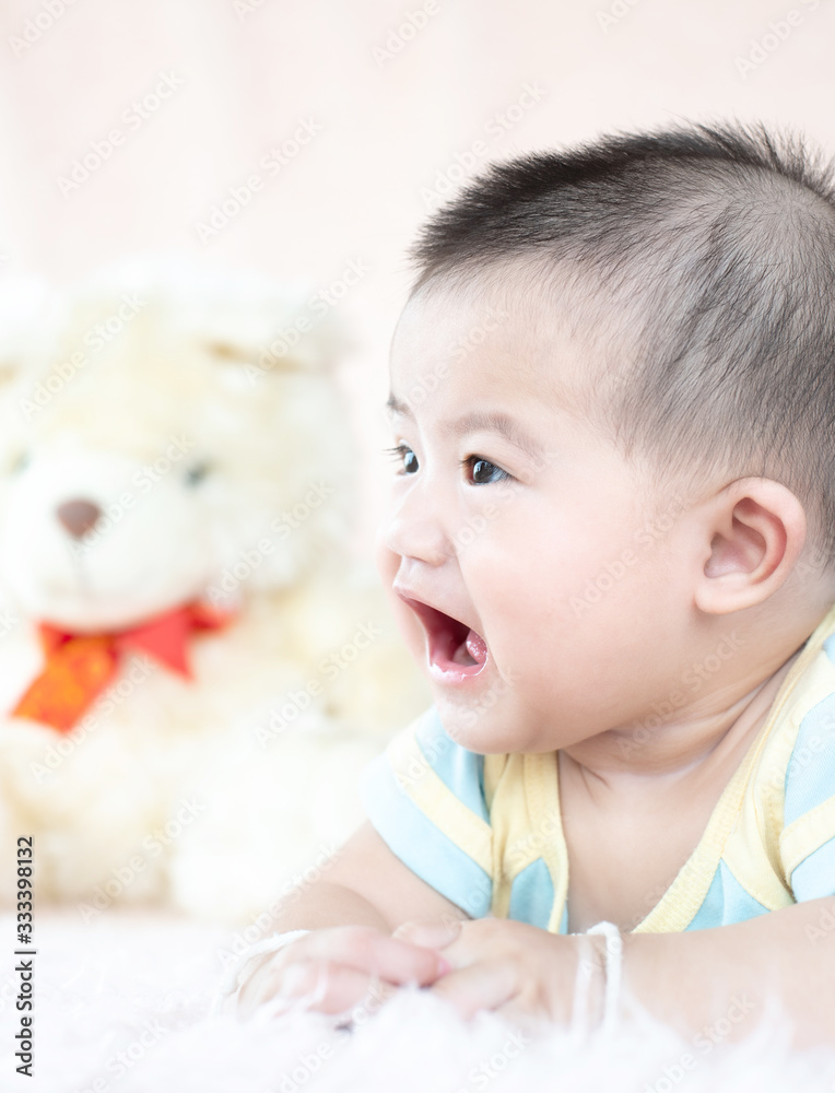 Closeup asian baby infant laying comfortably on bed playing with bear doll on softness cushion,Baby development concept. Closeup asian baby infant laying comfortably on bed playing with bear doll on softness cushion,Baby development concept.