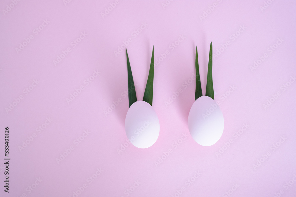 Two eggs with ears of leaves on a pink background.One leaf bent. top view. concept of minimalism eggs Two eggs with ears of leaves on a pink background.One leaf bent. top view. concept of minimalism eggs