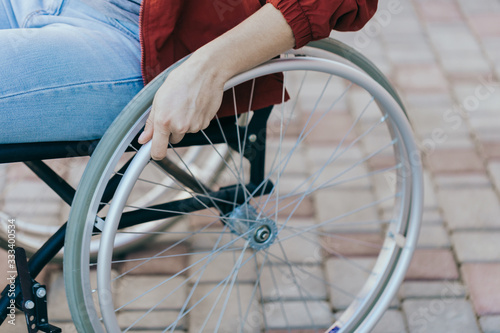 Close up of a young woman in a wheelchair while walking in a park on a sunny day. Recovery and healthcare concepts.