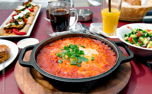 Traditional Middle Eastern dish of Shakshuka in a pan with salads and fresh bread.