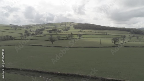 Aerial view flying above Welsh agricultural farmland meadow boundaries descending pull back photo