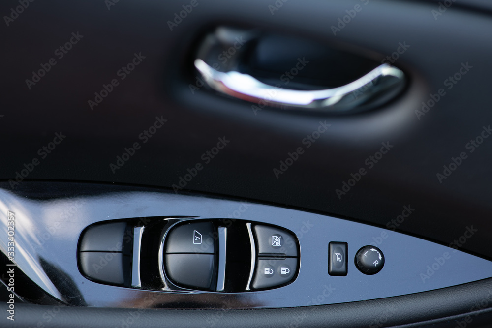 Detail on buttons controlling the windows in a car. Car interior details of door handle with windows controls and electric mirrors adjustments. Window and mirror control panel on driver's door