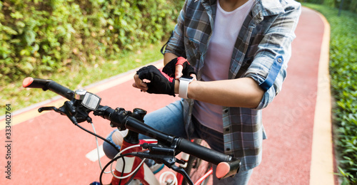 Woman riding mountain bike in park looking at her smartwatch