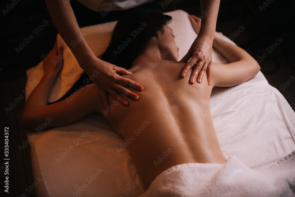 Obraz premium Professional massage therapist massages the back of young unrecognizable woman lying on massage table, close-up. Beautiful naked girl with perfect skin gets relaxing massage. Concept of body care.