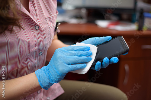 Safety and smartphone  covid-2019. Woman in the medical mask and gloves wiping the phone with a napkin