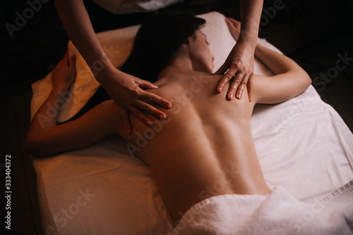 Professional massage therapist massages the back of young unrecognizable woman lying on massage table, close-up. Beautiful naked girl with perfect skin gets relaxing massage. Concept of body care.