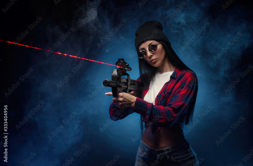 a girl in a checked shirt on a dark background with an automatic rifle