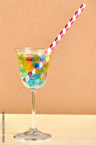 Striped straw, lush jelly balls and fizzy beverage inside elegant wine glass on the table. Party and Bar attributes. Backdrop for advertisement photo