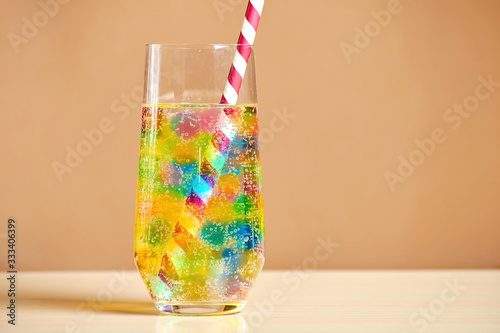 Multi-colored jelly balls and fizzy drink inside long cocktail glass with red-white straw. Backdrop and copy space. Bar and party equipment photo