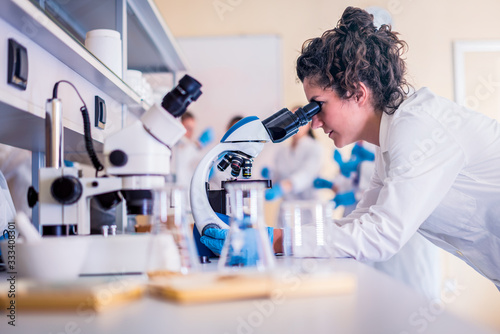 Leinwand Poster Young female scientist looking through a microscope in a laboratory doing resear