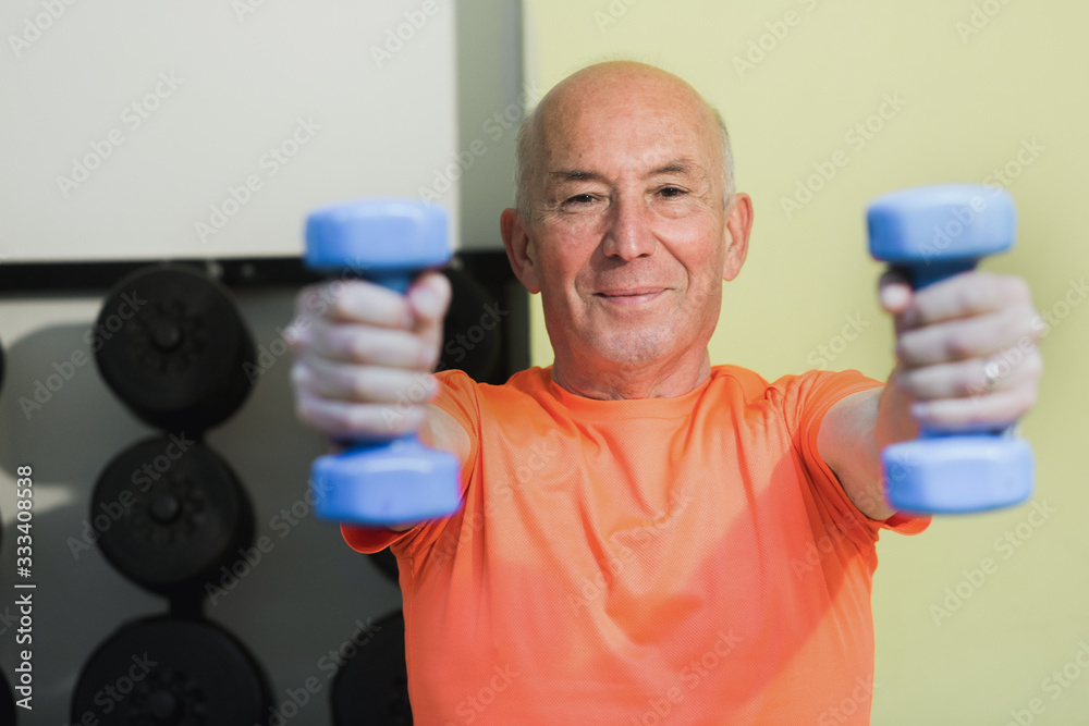 Anziano fa esercizio in palestra con i pesi Anziano fa esercizio in palestra con i pesi