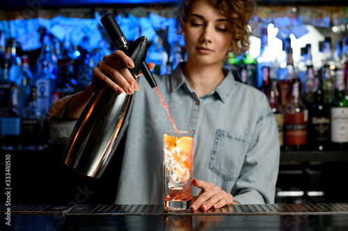 young bartender woman energetically pouring cocktail using steel siphon