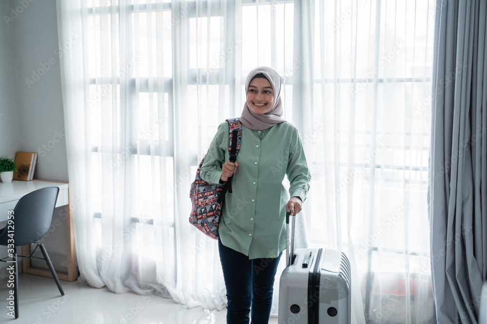 beauty young hijab traveler walk and carrying her bag and holding suitcase in the front windows with curtain