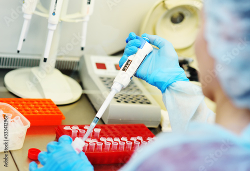 A young female scientist works in a sterile genetic or bacteriological laboratory with a dispenser and reagents in a medical gown, gloves and a doctor's cap.