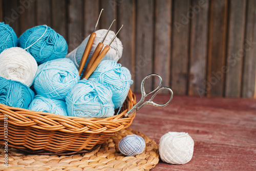 Women's hobby. Crochet and knitting. Working space. Blue yarn in basket,  knitting needles, scissors, crochet hooks on the wooden background in the cozy home in rustik style.