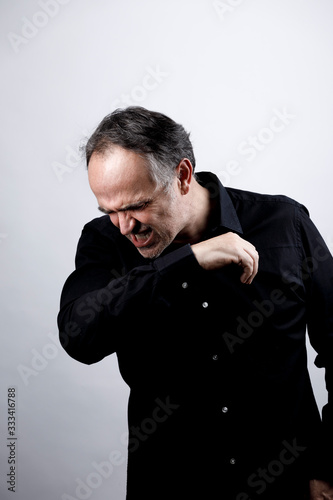uomo in camicia nera starnutisce e si ripara con il gomito, isolato su sfondo nero photo