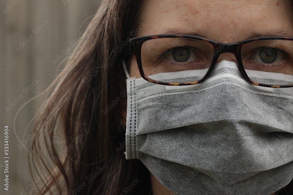 Young Australian woman wearing glasses and a paper surgical protective face mask to guard against catching or spreading infectious diseases and viruses in a public park, Victoria, Australia